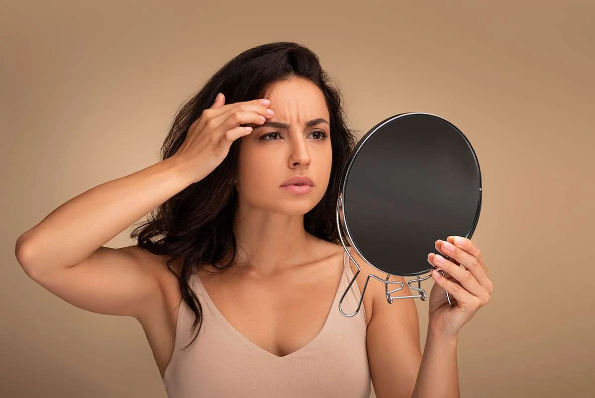 Woman checking fine lines and skin elasticity in a mirror